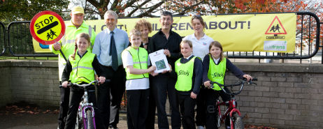 Mixture of school children, teachers and lollipop man standing at the front of a school in two lines